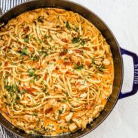 A sauté pan with creamy Cajun seasoned chicken and pasta with crispy pancetta, cream, garlic, and parsley.