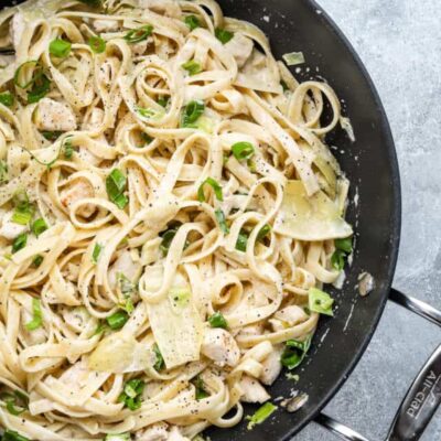 Closeup of creamy chicken pasta with artichokes and green onions.