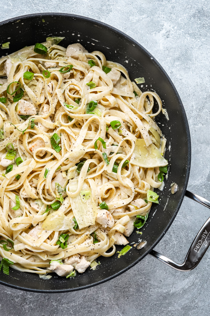 Closeup of creamy chicken pasta with artichokes and green onions.