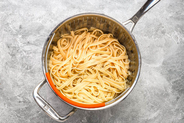 Drained fettuccine in preparation of creamy chicken pasta with artichokes.