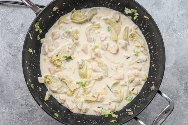 Creamy chicken pasta prep: chicken broth, cream, and artichokes are added to the dish.