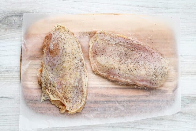 Seasoned raw chicken breasts on parchment paper.
