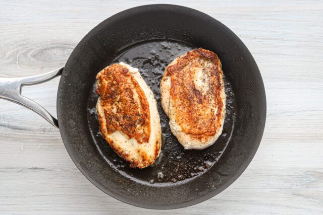 Chicken breasts in the skillet showing crispy skin, ready to bake.