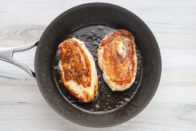 Golden browned chicken breasts frying in a black skillet.