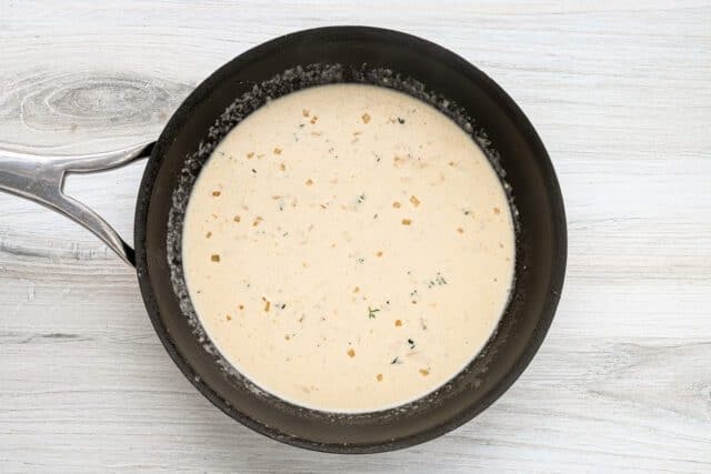 Creamy soup with herbs in a black saucepan.