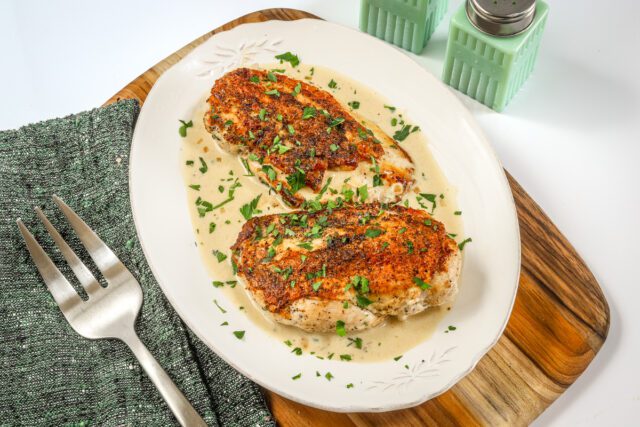 Creamy Dijon chicken breasts are arranged on a serving tray with the white wine sauce.