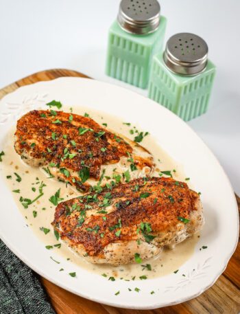 Creamy Dijon chicken breasts are arranged on a serving tray with the white wine sauce.
