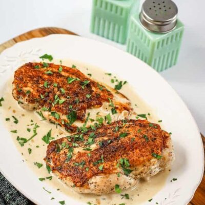 Baked chicken breasts topped with herbs and spices on a white plate.