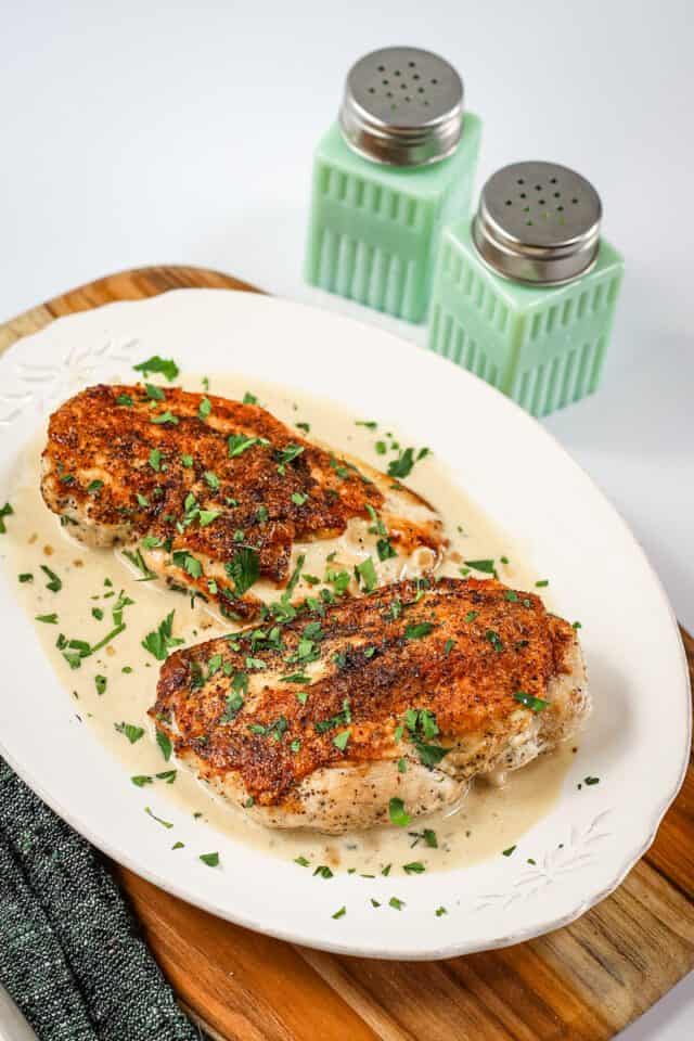 Baked chicken breasts topped with herbs and spices on a white plate.
