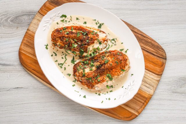 Creamy Dijon chicken breasts are arranged on a serving tray with the white wine sauce.