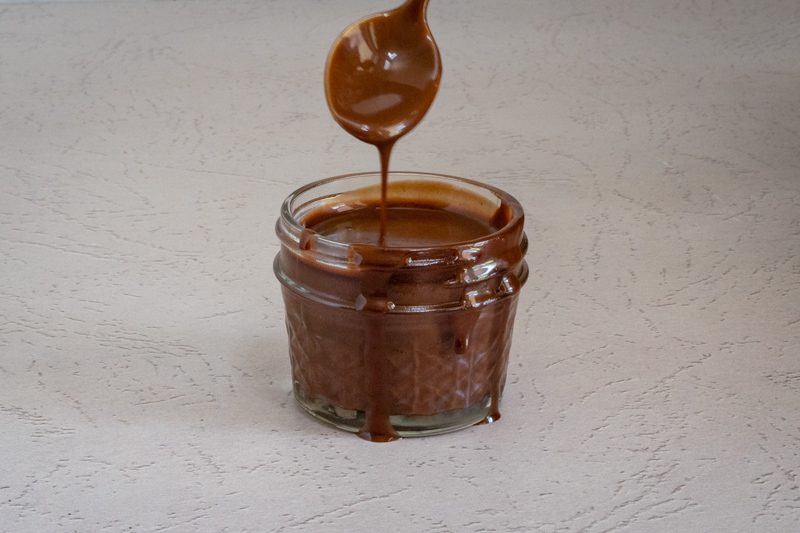 dripping chocolate sauce (keto, sugar-free) from a spoon into a jar