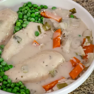 Cooked chicken with vegetables in a creamy white sauce, served with green peas.