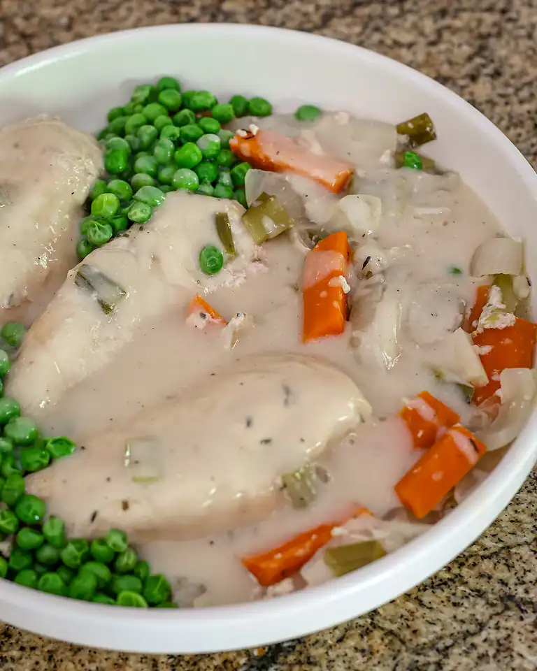 Cooked chicken with vegetables in a creamy white sauce, served with green peas.
