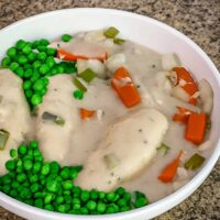 A serving bowl with slow cooker chicken breast meal with creamy sauce, carrots and peas.
