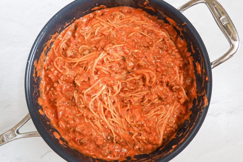 Adding the drained spaghetti to the tomato sauce and beef mixture.