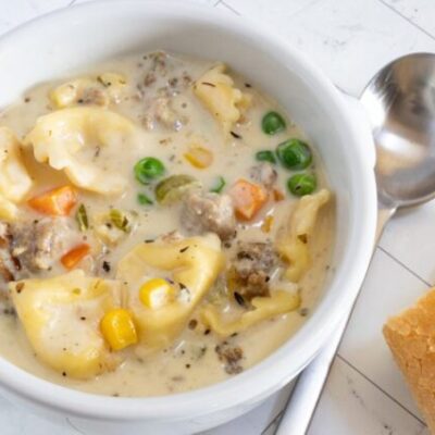 A bowl of sausage and tortellini soup with bread on the side.