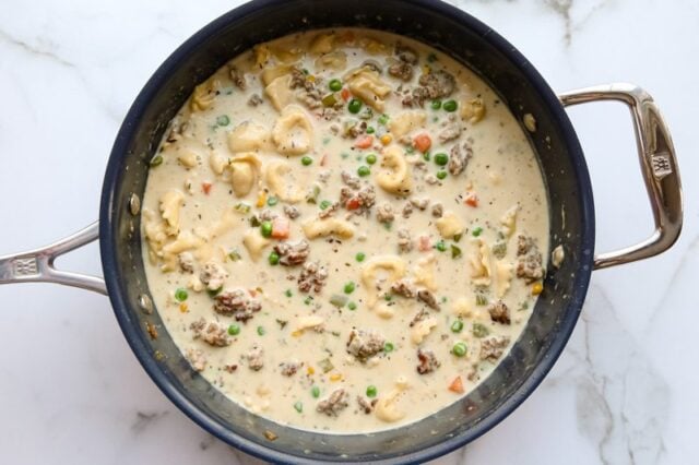Finishing creamy tortellini and sausage soup with cream and vegetables.