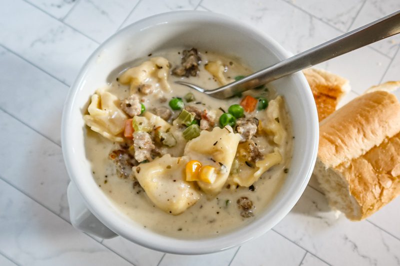 creamy sausage tortellini soup in a bowl with bread and a spoon