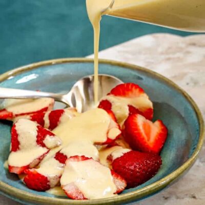 Fresh strawberries with creamy vanilla sauce being poured over them.
