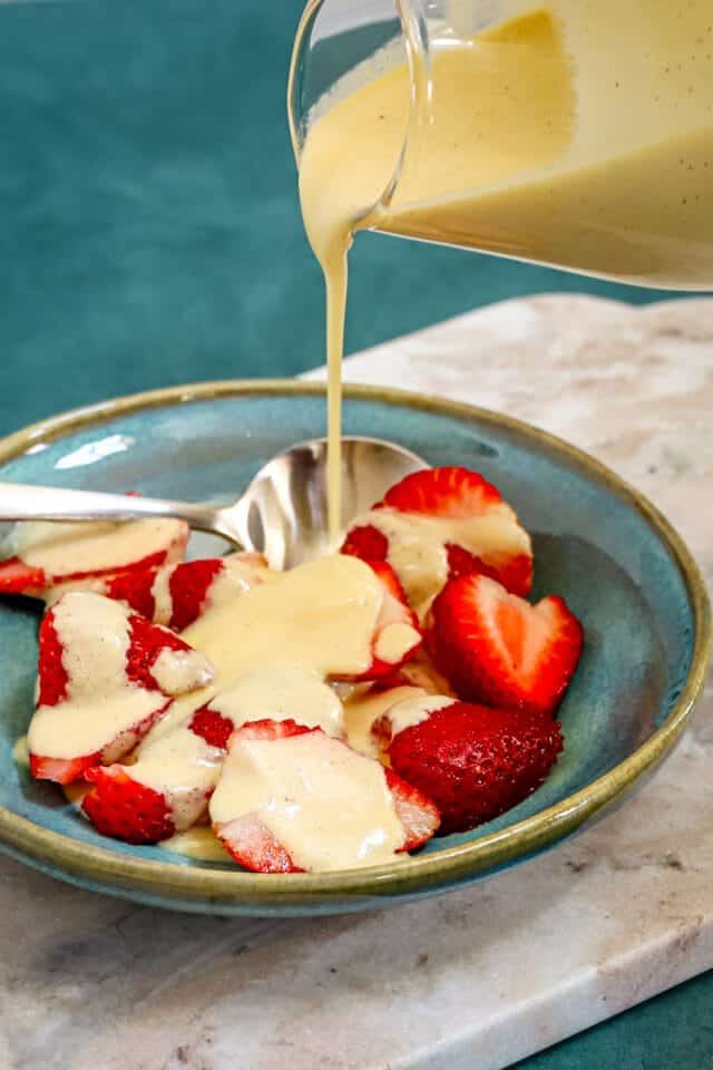 Fresh strawberries with creamy vanilla sauce being poured over them.