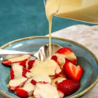 Creamy custard being poured over fresh strawberries in a bowl.