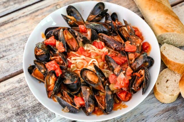 Creole style mussels with tomatoes and linguine in a wide shallow bowl.