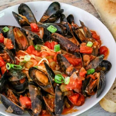 A bowl of mussels with Creole sauce, linguine, and a baguette on the side.