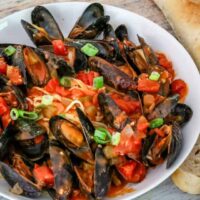 A bowl of mussels with Creole sauce, linguine, and a baguette on the side.