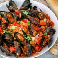 A bowl of mussels with Creole sauce, linguine, and a baguette on the side.