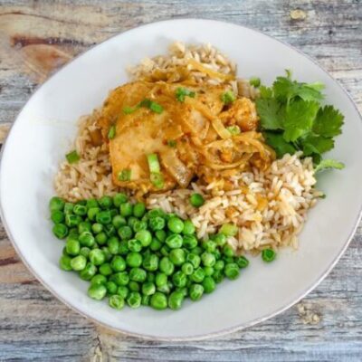 slow cooker chicken with curry flavor on a plate with rice and peas