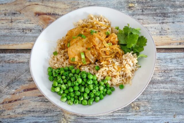 slow cooker chicken with curry flavor on a plate with rice and peas