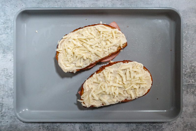 topping the assembled croque monsieur sandwich with more bechamel and cheese