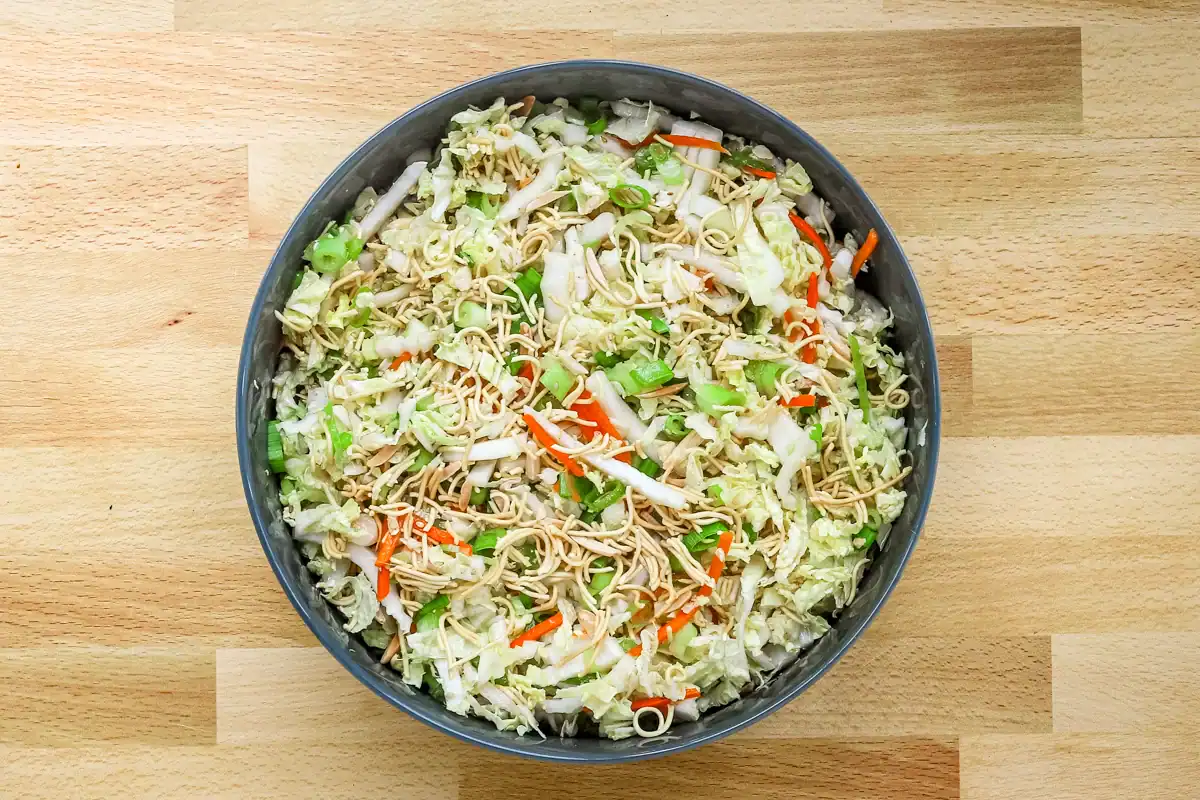 Stir-fried vegetable and noodle salad in a gray bowl on wooden surface.