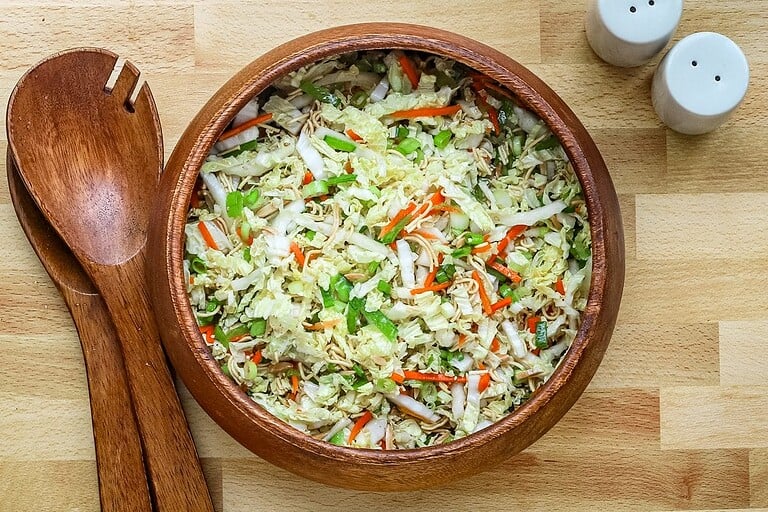 Fresh vegetable salad in wooden bowl with wooden scoop on side and salt and pepper shakers in background.