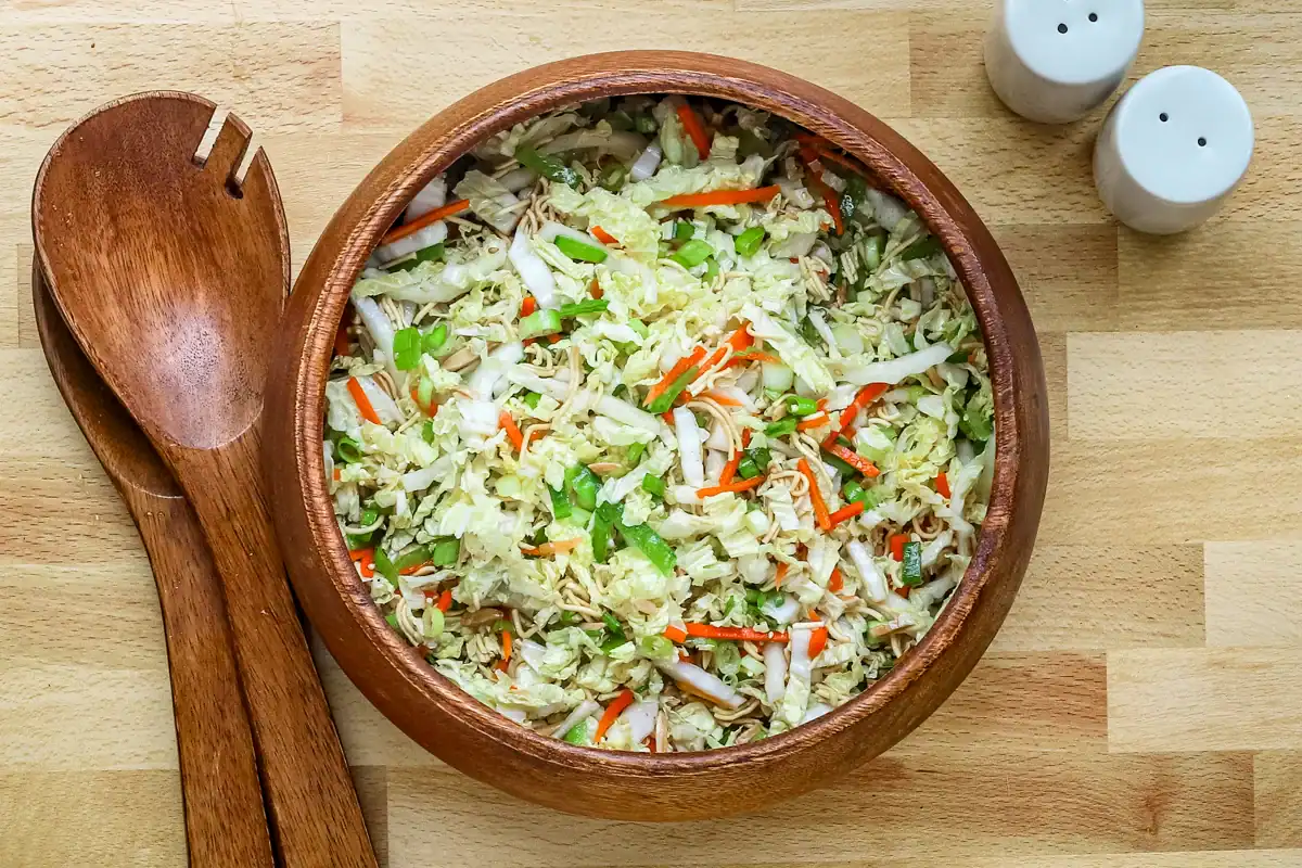 Fresh vegetable salad in a wooden bowl with chopped cabbage, carrots, and green onions.