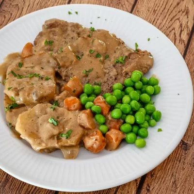 Fried chicken with gravy, and green peas on a white plate.