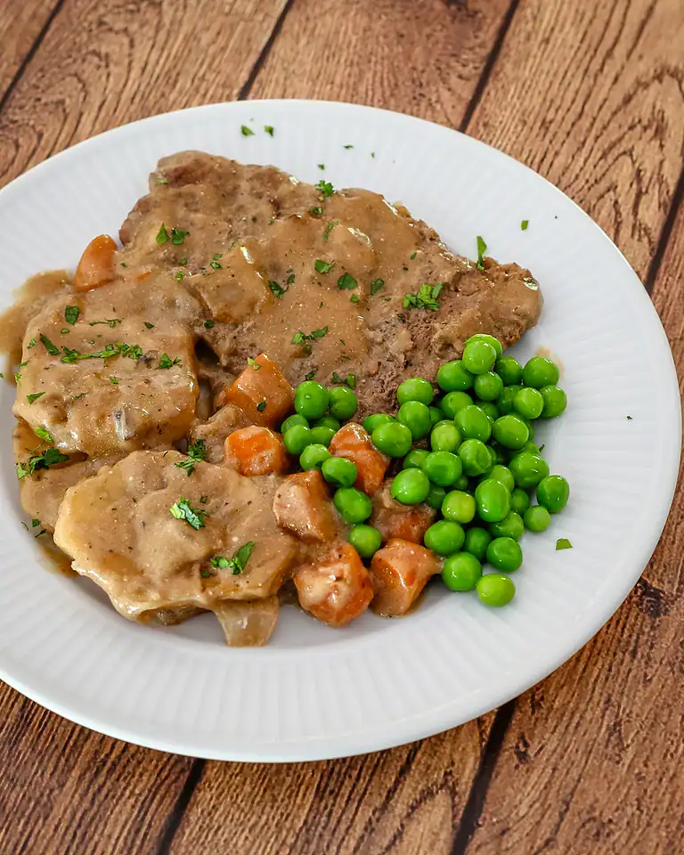 Fried chicken with gravy, and green peas on a white plate.
