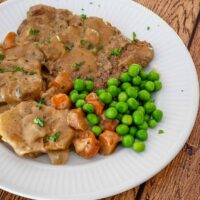 Cube steaks on a plate with mushroom gravy, carrots, potatoes, and peas.