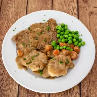 Roast beef with brown gravy, green peas, and glazed carrots on a white plate.