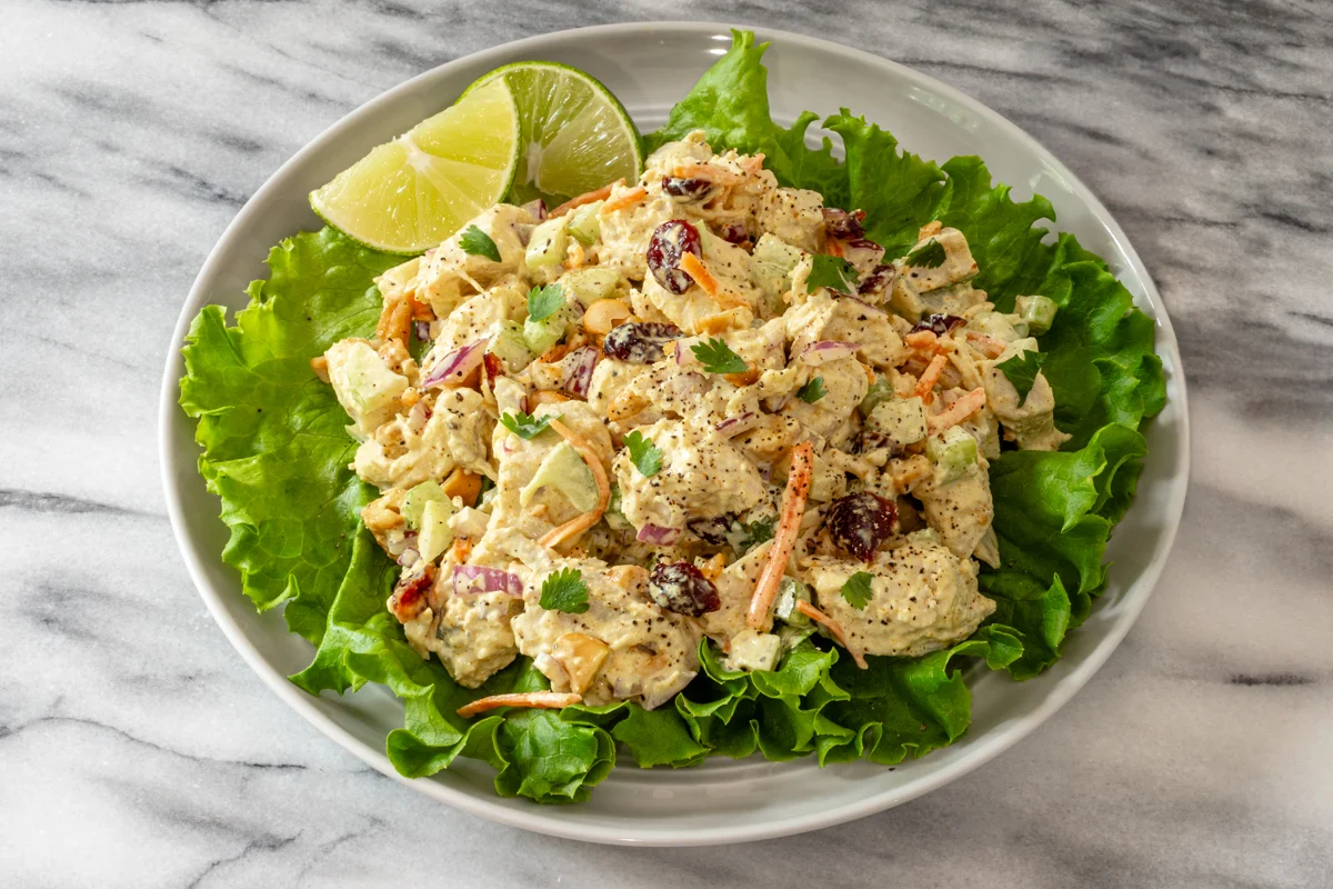 Curried chicken salad on a lettuce-lined plate with parsley and lime wedges.