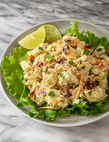 Curried chicken salad on a lettuce-lined plate with parsley and lime wedges.