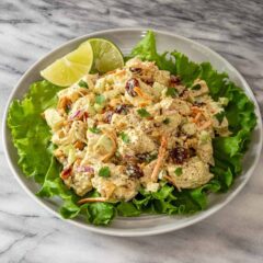Curried chicken salad in a bowl on a bed of lettuce with lime wedges.