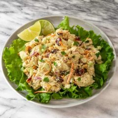 Creamy chicken salad with fresh vegetables and herbs on a white plate.