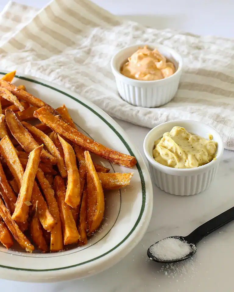 Golden crispy French fries with two dipping sauces on side.