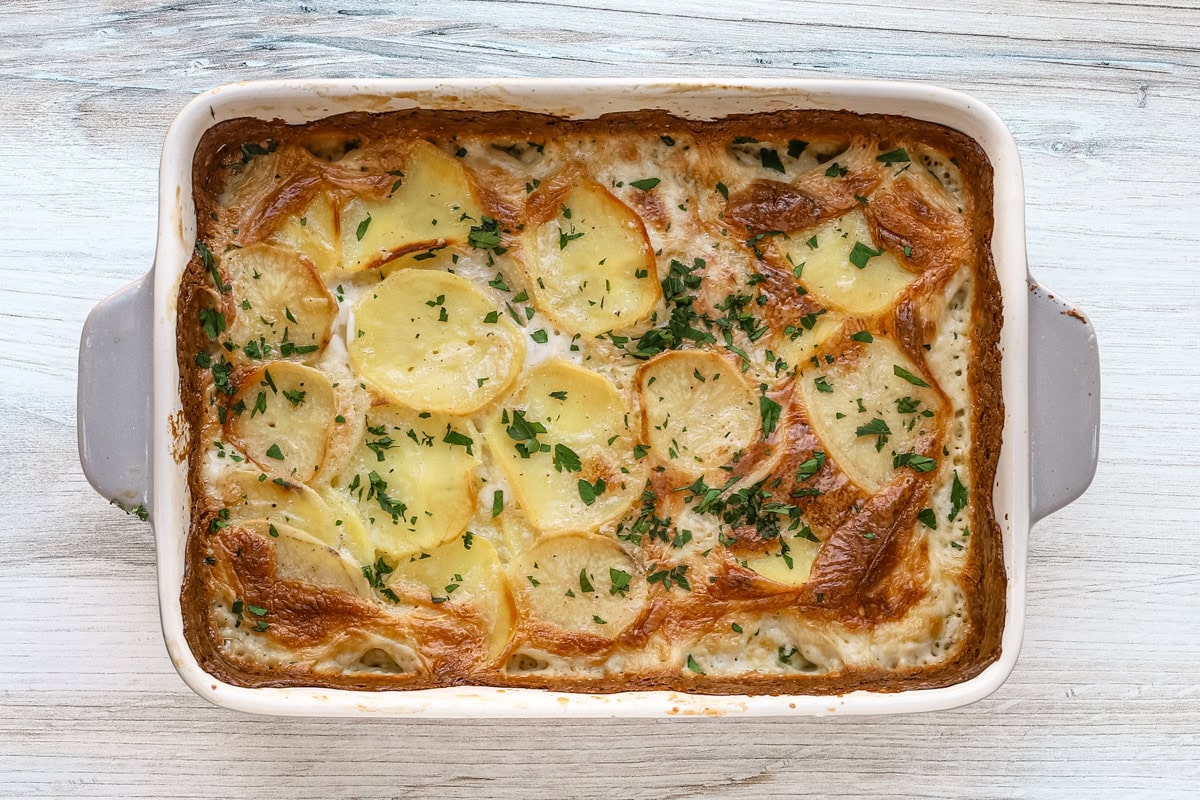 A baking dish with potatoes Dauphinoise with parsley garnish.