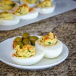 deviled eggs with crisp bacon on a plate with olives