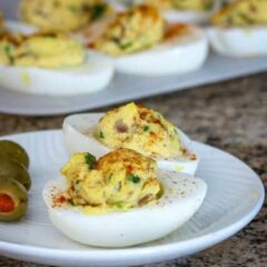 deviled eggs with bacon on a plate with more in the background