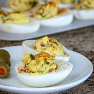 deviled eggs with bacon on a plate with more in the background