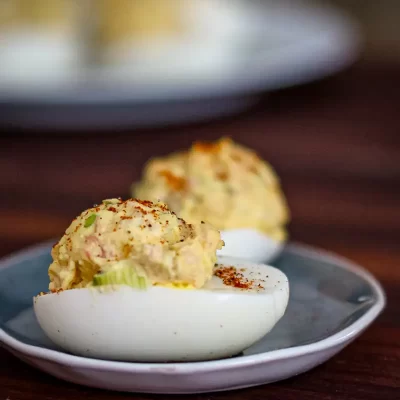 Creamy deviled eggs topped with paprika on a white plate.