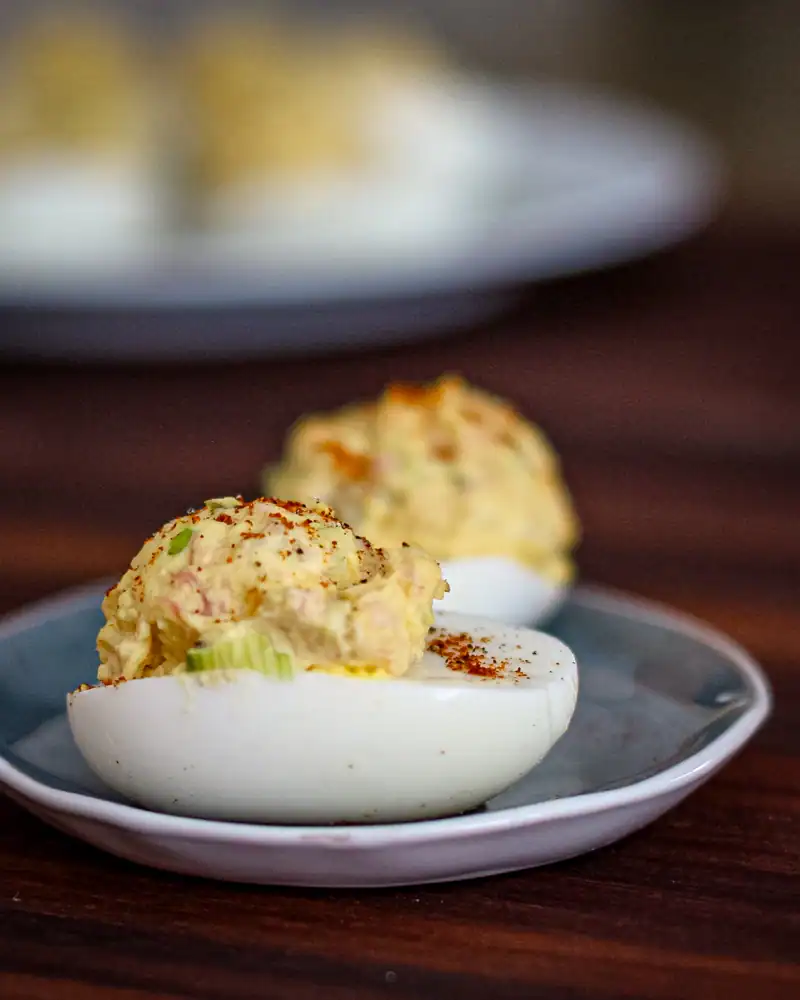 Creamy deviled eggs topped with paprika on a white plate.